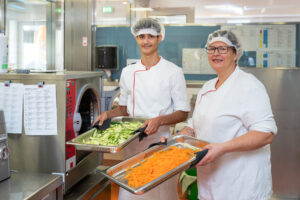 Zwei Personen des Küchenpersonals halten Behälter mit Karotten und Zucchini