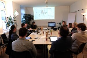 Projektteam und Eigentümer:innen sitzen an einem Tisch, schauen auf eine Karte und unterhalten sich über Lösungen